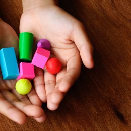 hands holding plastic 3D shapes to help with learning school topics